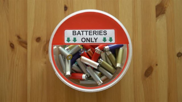 Many hands putting lot of used batteries in the recycling box. Top view. Close up