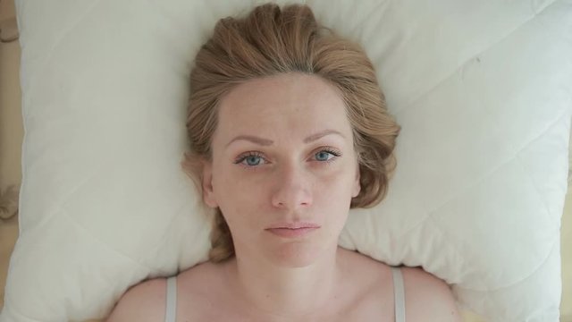 A woman lies on the bed and sharply opens her eyes, looks into the camera. Close-up. View from above