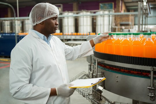 Male worker examining bottles in juice factory