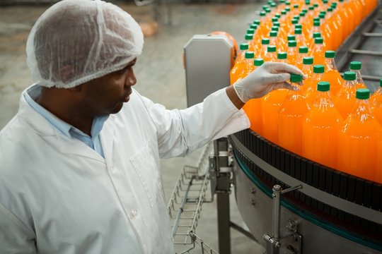 Serious male worker examining bottles in juice factory