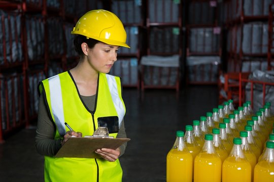 Female worker examining juice bottles in factory