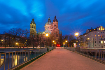 Obraz premium Saint Lucas Church, the largest Protestant church in Munich, and bridge across Isar River at night, Bavaria, Germany