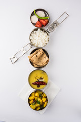 indian typical stainless steel lunch box or tiffin with north indian or maharashtrian food menu like chapati//roti, dal tadka, white rice and aloo / potato sabji / gobi or cauliflower sabji with salad © StockImageFactory