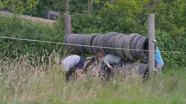  Competitors in endurance race, teammates helping each other through tyre obstacle. 
