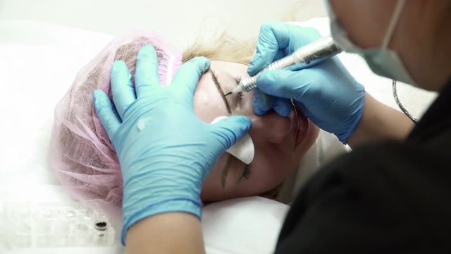 Closeup of beautician is making an eyebrow permanent makeup for a woman