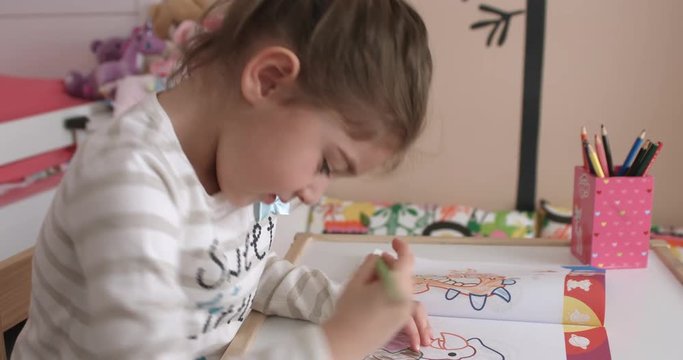 Cute little girl coloring then looking at camera, her room can be seen in the background