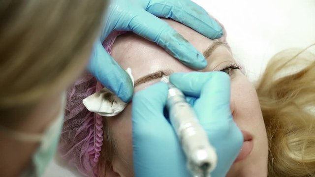 Closeup of cosmetologist is making an eyebrow permanent makeup in beauty salon
