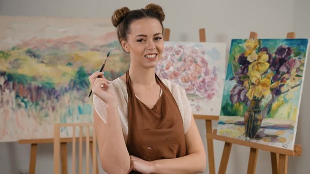 Smiling happy painter with a paintbrush in hands posing on camera in art studio.