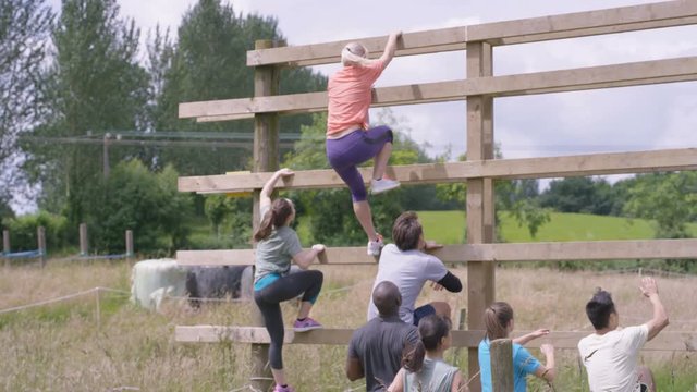  Competitors in endurance race, teammates helping each other climbing wall. 