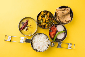 indian typical stainless steel lunch box or tiffin with north indian or maharashtrian food menu like chapati//roti, dal tadka, white rice and aloo / potato sabji / gobi or cauliflower sabji with salad