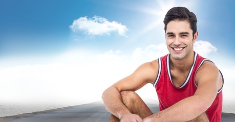 Male runner sitting on road against sky and sun