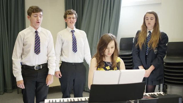  Teen group singing & teacher playing keyboard in school music lesson