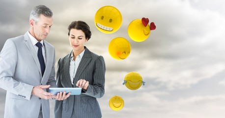 Fototapeta na wymiar Business people with tablet against cloudy sky with emojis