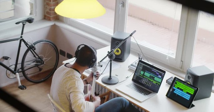 black man creative musician at home studio works by playing,singing and recording guitar with notebook tablet and microphone indoor in modern industrial house. 4k handheld top view overhead video shot
