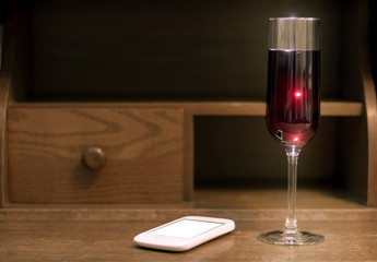 Red wine in wine glass with lights behind on wooden table and white mobile phone.
