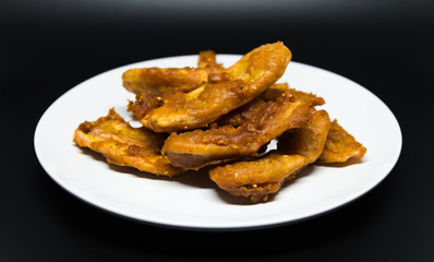 Delicious traditional golden fried banana fritters on white plate with black background isolated