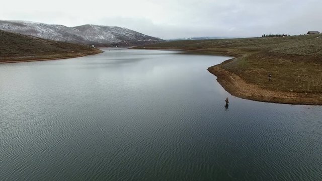 Flying over lake backwards as you pass man fly fishing in lake