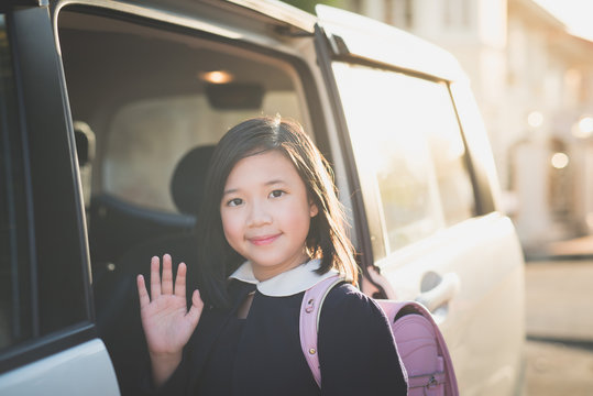Asian girl in student uniform going to school by car and  waving goodbye
