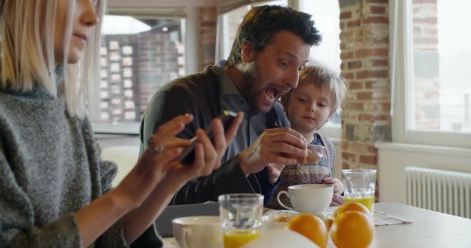 modern family little girl having breakfast with dad while mom uses smartphone and works indoor in modern industrial house. caucasian. 4k handheld slow motion video shot