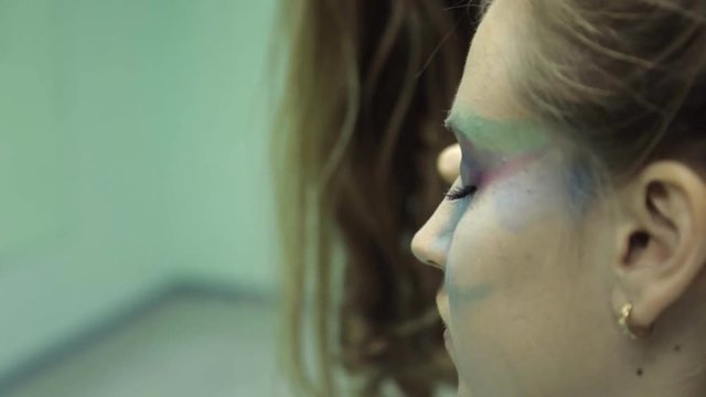 Artist does make-up on young girl, close up, body-art. Stylist draws in bold lines by means of shadows and a brush which remind beak and plumage of beautiful bird on female features. The professional