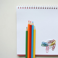 Paper clips and colorful pencils on blank sketch book page.