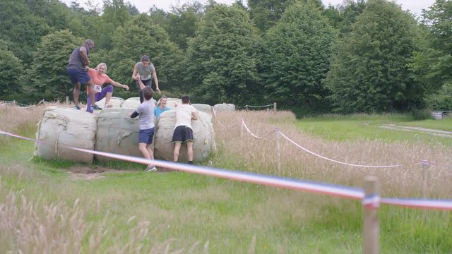  Competitors in assault course race, males helping female team members over obstacles. 
