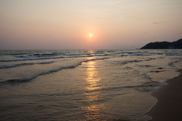 Soft wave of blue ocean on sandy beach at sunset.