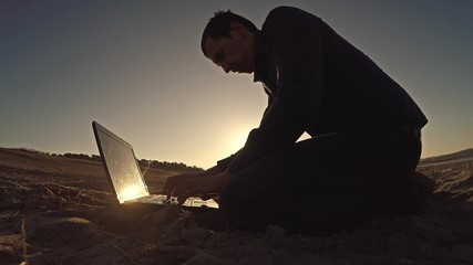 man businessman laptop freelancer working behind sitting on beach freelancing silhouette in the sun