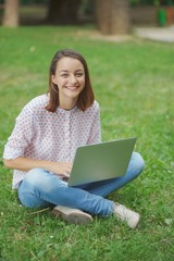 Young woman with laptop sitting on green grass