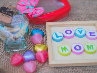 Fototapeta na wymiar love mom spelled with colorful alphabet blocks and a red heart isolated on wooden board and sack - Mothers Day