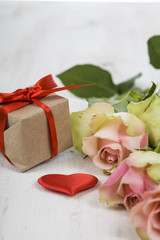 Pink roses, gift and hearts on a wooden background.