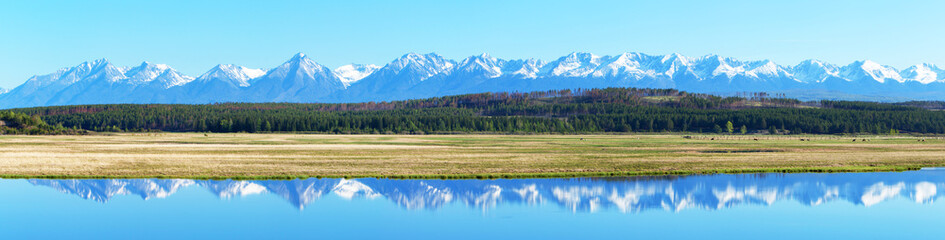 Panorama of spring landscape with the reflection of the snow-capped Eastern Sayan Mountains in the river