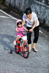 Fototapeta premium Asian Chinese little girl riding bicycle with mom guide