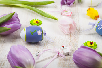 Bouquet purple tulips and Easter eggs on a light wooden table.