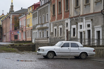 Fototapeta na wymiar Old white Volga car parked on a cobbled side street in Kamianets-Podilskyi, Western Ukraine. The street is still wet from recent rains