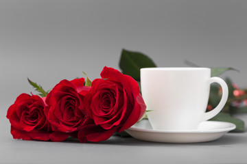 Obraz na płótnie Canvas Red roses with a coffee cup of white color on a gray background