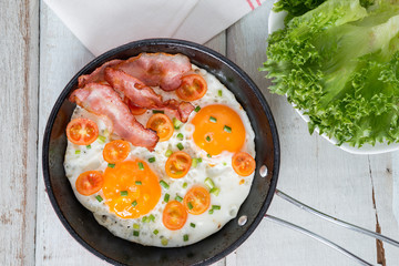 Pan of fried eggs, bacon and tomato. Top view.