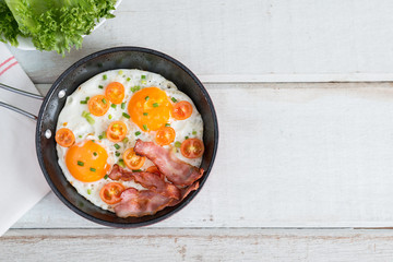 Pan of fried eggs, bacon and tomato. Top view.