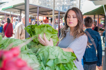 Young woman on the market. Happy young brunette  picking some vegetables. Portrait of beautiful young woman choosing green leafy vegetables