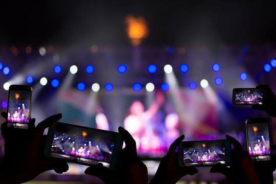 Silhouette of hands using camera phone to take pictures and videos at live concert.