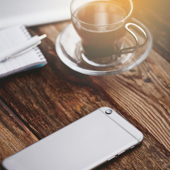 Smartphone and cup of coffee on the wooden table.