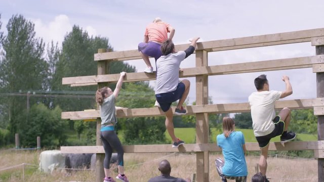  Competitors in endurance race, teammates helping each other climbing wall. 