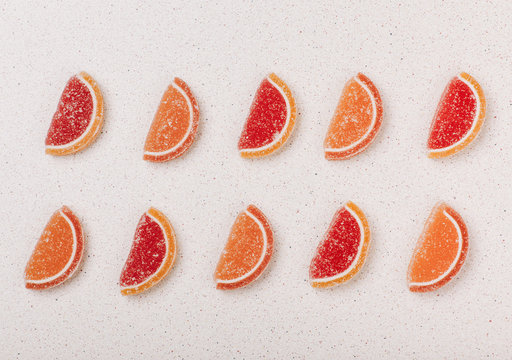 Slices Of Orange And Grapefruit From Marmalade Laid Out In A Pattern In Two Rows On A Gray Background.