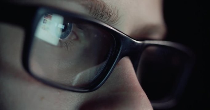 12 years teen puberty eye glasses looking at the monitor in a dark room,surfing the Internet, close-up