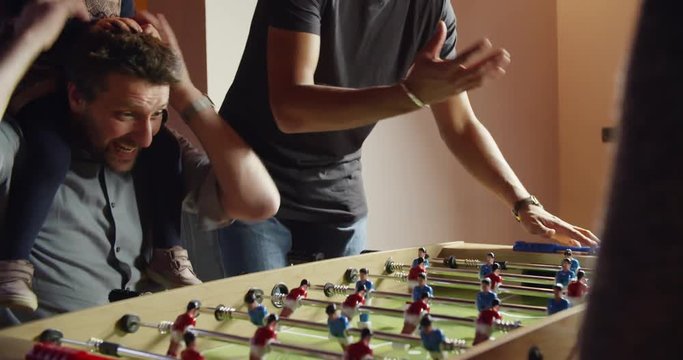 multiethnic group of friends and child playing table football. indoor in modern industrial house. 4k handheld slow motion detail video shot