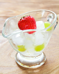 Juicy strawberry in a glass container with ice on a wooden surface. Selective focus