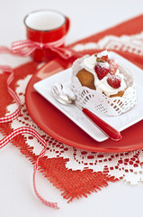 Baba with a cream and strawberries in white and red plates and red cup with ribbon on napkin on wooden board