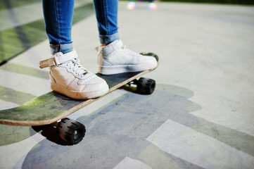 Legs of teenage urban girl on skateboard at skate park on the evening.