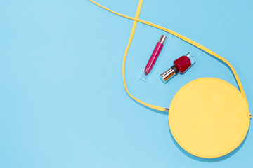 Round yellow purse, red nail polish, red lipstick on a pastel blue background.