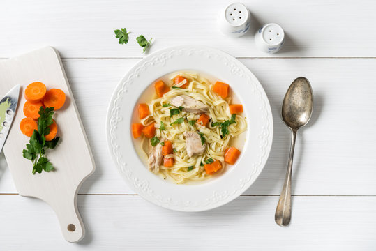 Top view of chicken soup with pasta, carrot and parsley on white table